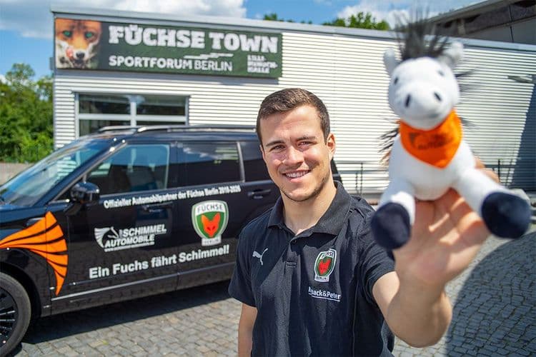 Tim Freihöfer, jugador del Füchse Berlin, se para delante de un Hyundai SANTA FE y sostiene en la mano un pequeño peluche de caballo gris.