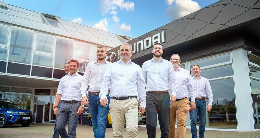 gruppenbild 7 automobilverkäufer dynamisch mit weißem hemd vor autohaus